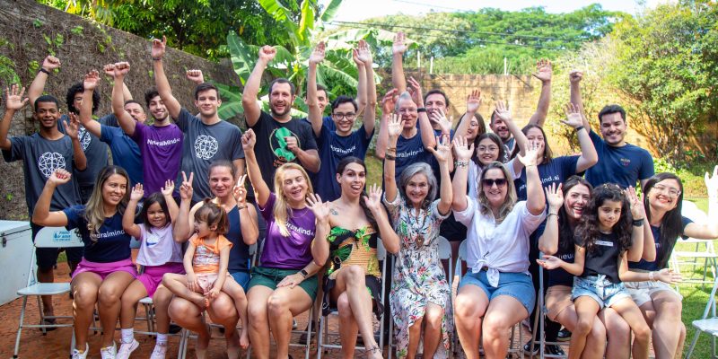 Mulheres e Homens que fazem parte da NeuralMind reunidos em uma foto, alguns sentados e outros em pé, com os braços para cima como se estivessem comemorando